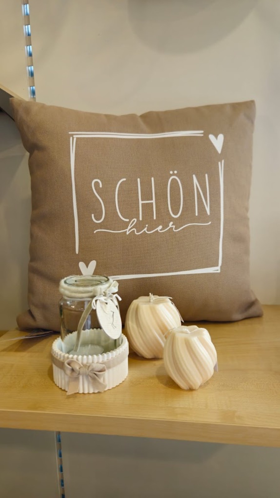 Kissen mit Aufdruck, Kerzen und Windlichter auf einem Regalbrett